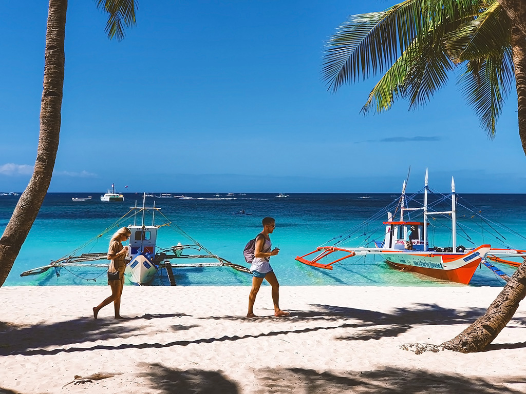 Tourists walking by the beach with boats parked at Boracay Island. Best Summer Destinations in Philippines